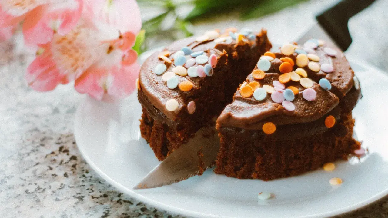Schokoladenkuchen mit bunter Streusel-Deko, ein köstliches Dessert, um Kuchenreste zu verwerten. Daneben zarte rosa Blüten.