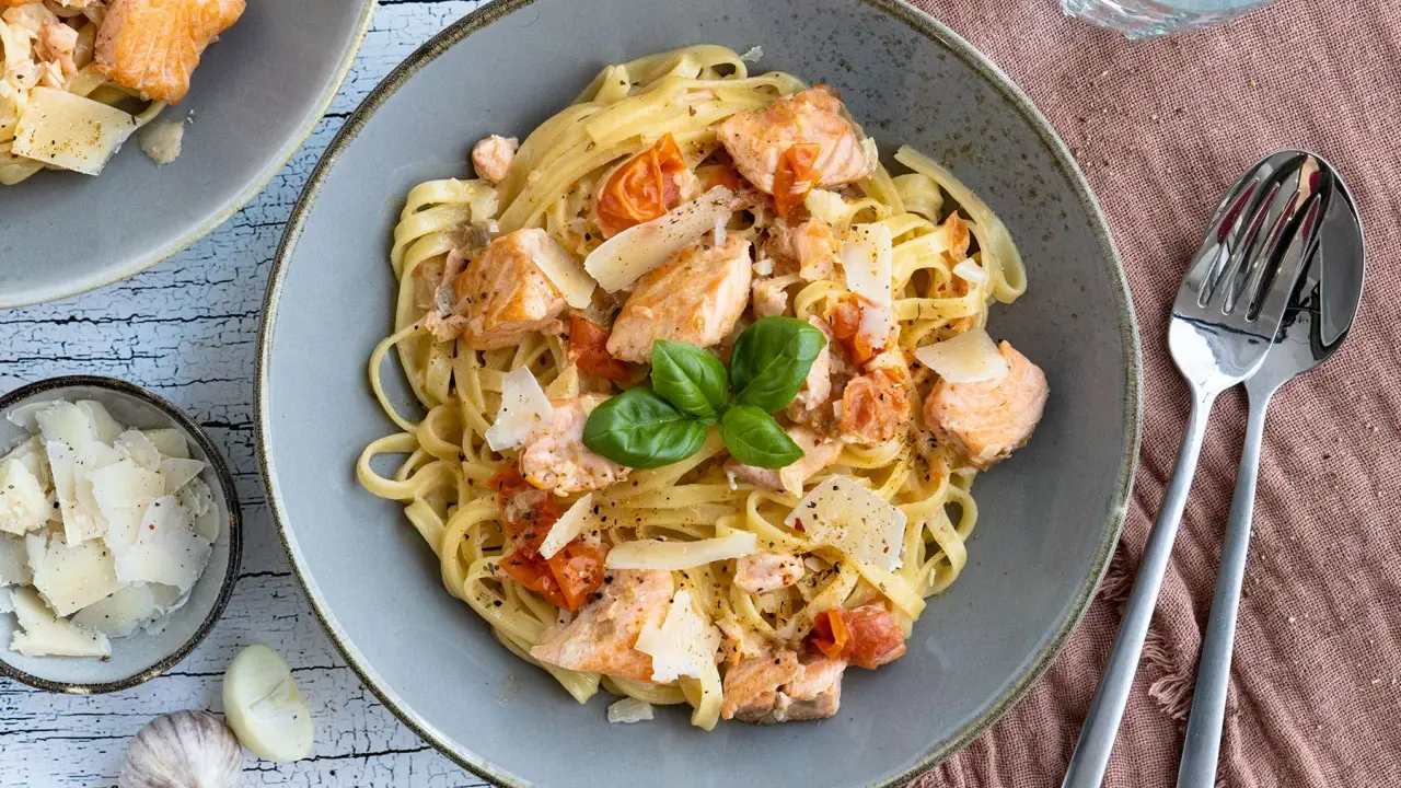 Tagliatelle al salmone mit Kirschtomaten und Parmesan, garniert mit Basilikum. Ein köstliches Gericht, das Lust auf mehr macht.