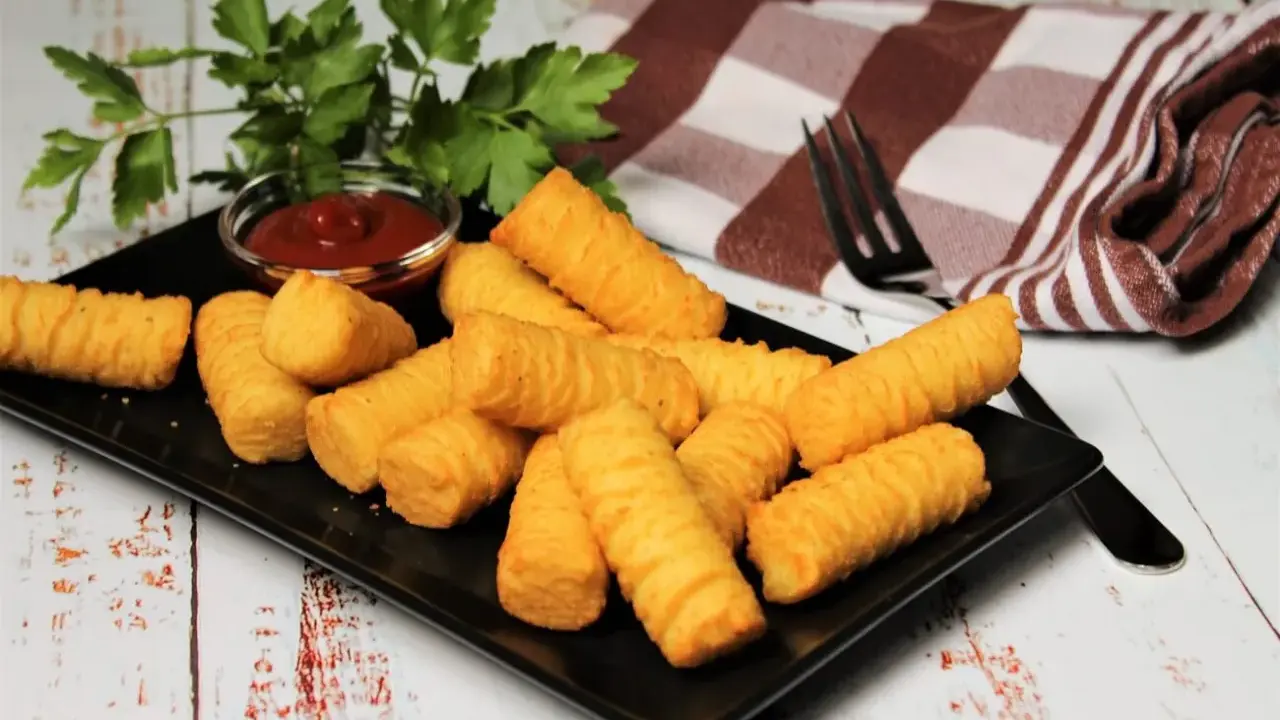 Goldbraune Kroketten, frisch zubereitet, liegen auf einem schwarzen Teller. Dazu gibt es Ketchup und frische Petersilie. Perfekt zum kroketten selber machen!
