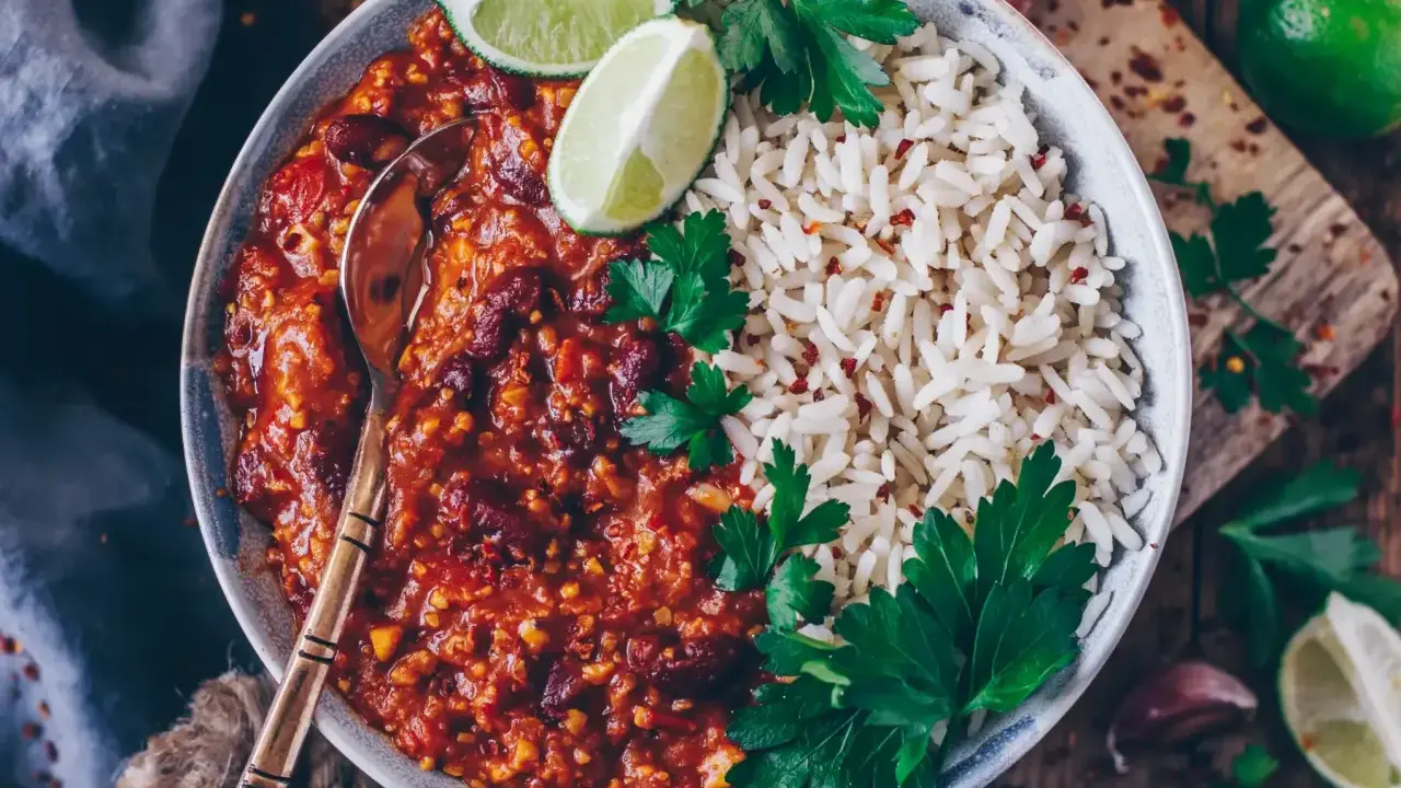 Herzhaftes Chili sin Carne mit Kidneybohnen, Reis, Limettenspalten und Petersilie. Ein Löffel wartet schon.