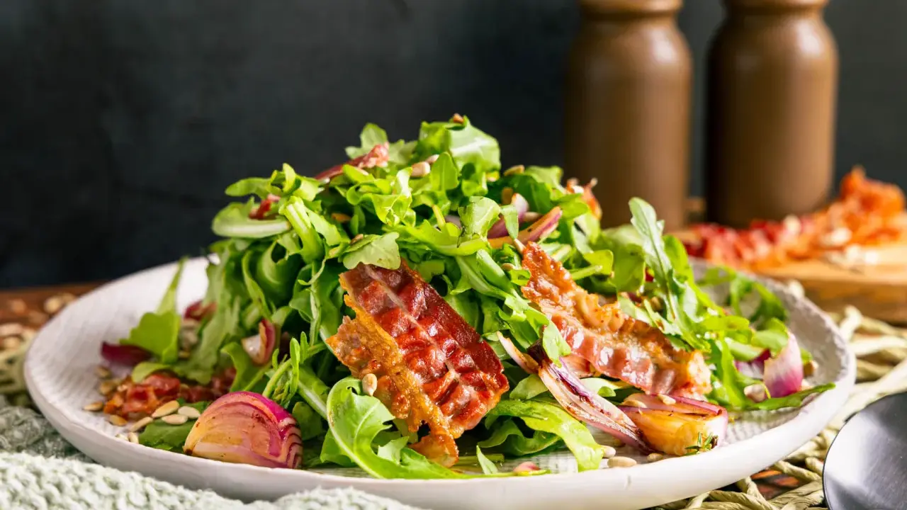 Salat mit Rucola, roten Zwiebeln und knusprigem Speck. Perfekte warme Beilagen zum Salat, die für zusätzlichen Geschmack sorgen.