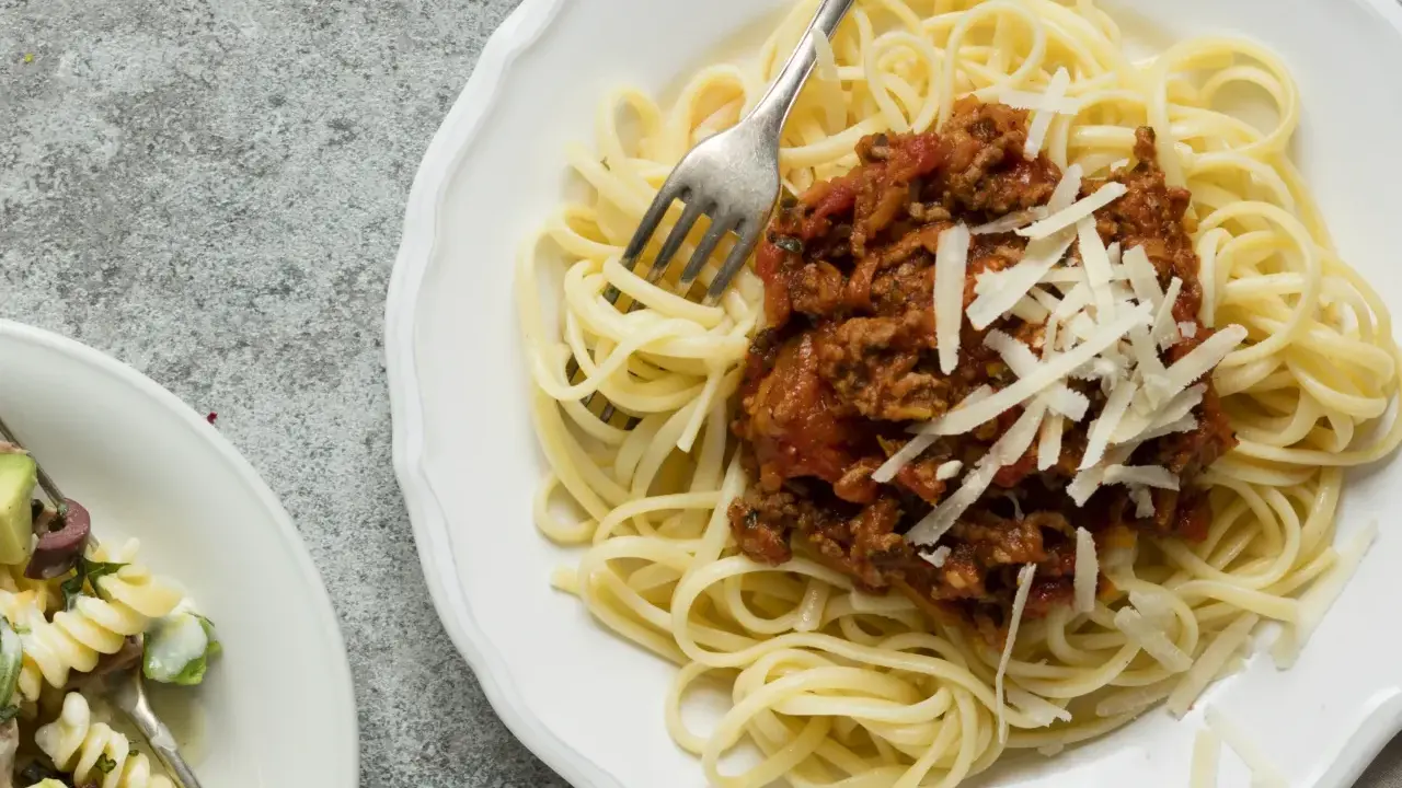 Ein Teller Spaghetti Bolognese, wie nach Omas Rezept, mit frisch geriebenem Parmesan. Daneben ein kleinerer Teller mit Nudelsalat.