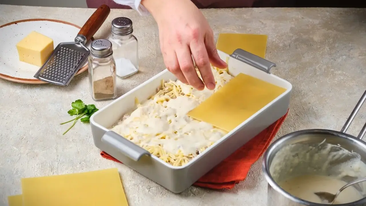 Hände legen Lasagneplatten auf eine Schicht Käse und Sauce. Ein Schritt im Lasagne rezept.