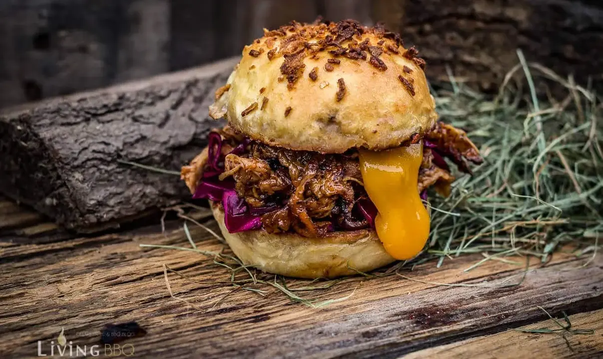 Saftiger pulled chicken burger mit geschmolzenem Käse und Rotkohl auf rustikalem Holz.