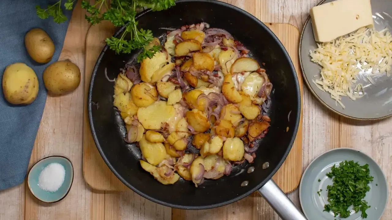 Bratkartoffeln mit Zwiebeln und Käse in der Pfanne. Man muss bratkartoffeln vorher kochen, damit sie schön knusprig werden. Dazu gibt es frische Petersilie und Salz.