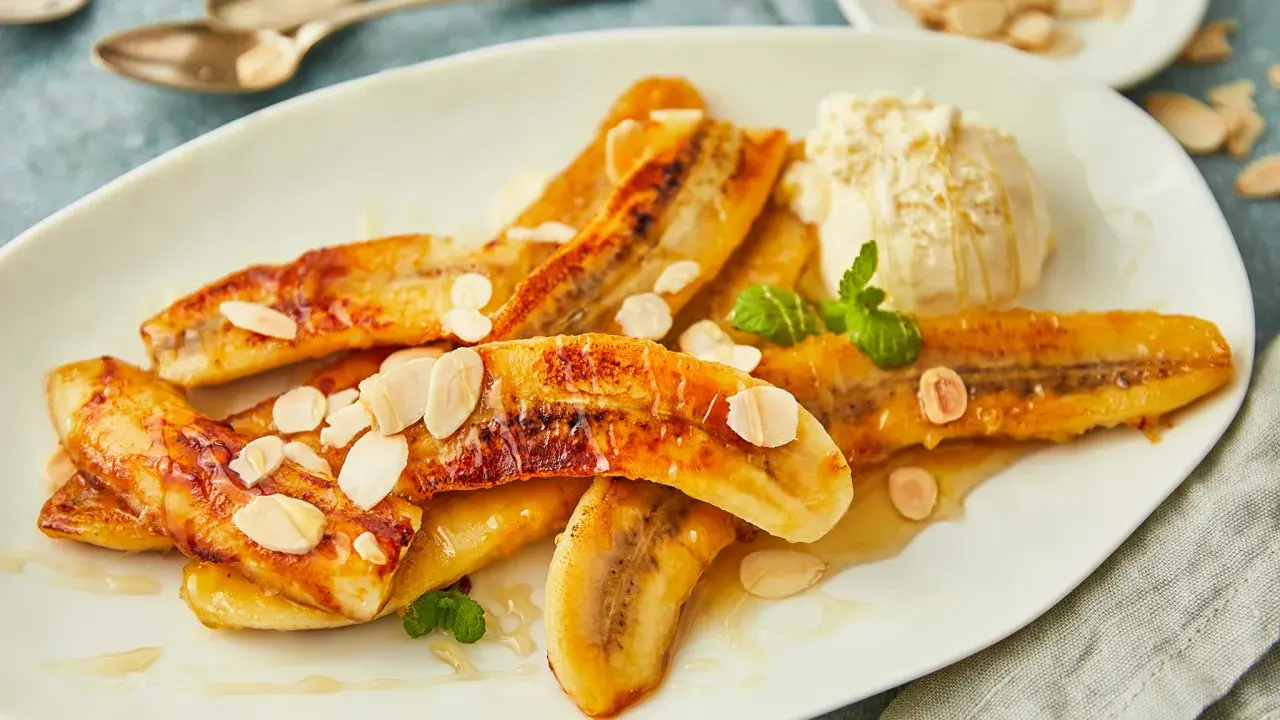 Gebackene Bananen mit einer Kugel Eis, garniert mit Mandelblättchen und Minze. Ein süßer Genuss!