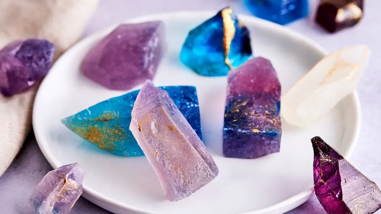 Bunte, essbare Kristalle selber machen: glitzernde Zuckerstücke in Blau, Lila und Weiß mit goldenen Akzenten auf einem Teller.