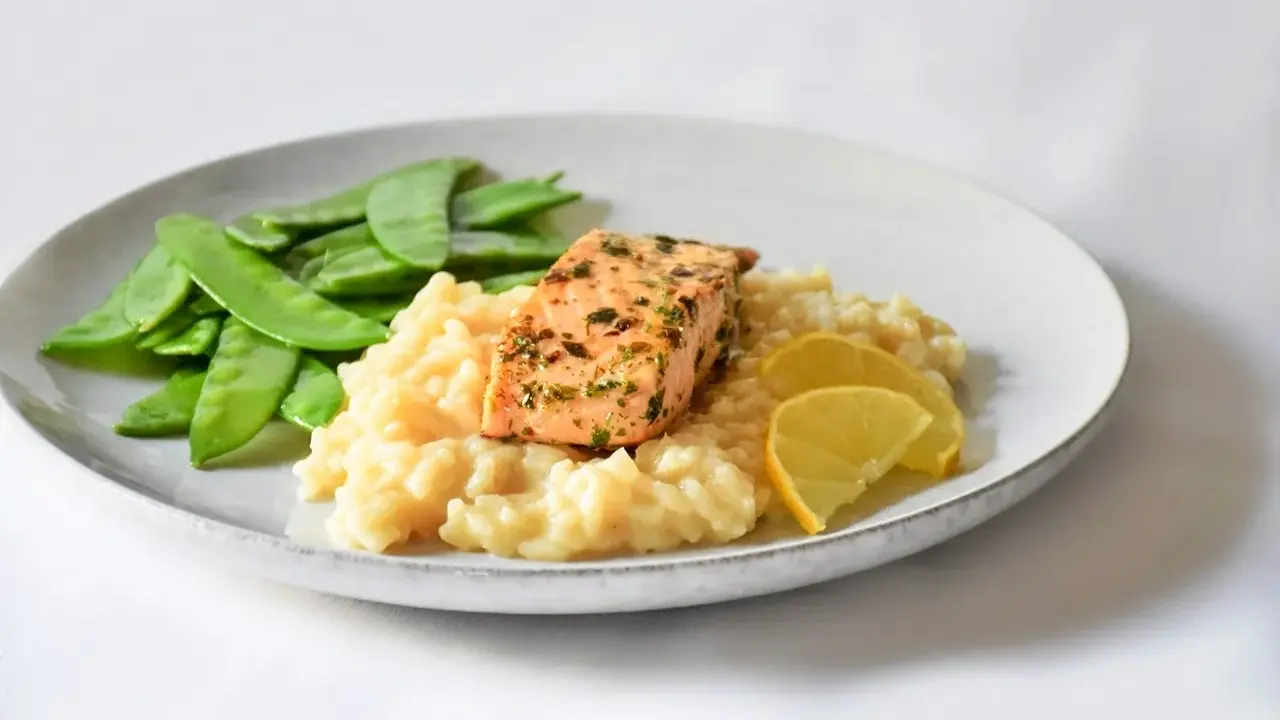 Ein Stück Lachs auf cremigem Zitronenrisotto, garniert mit Zuckerschoten und Zitronenspalten.