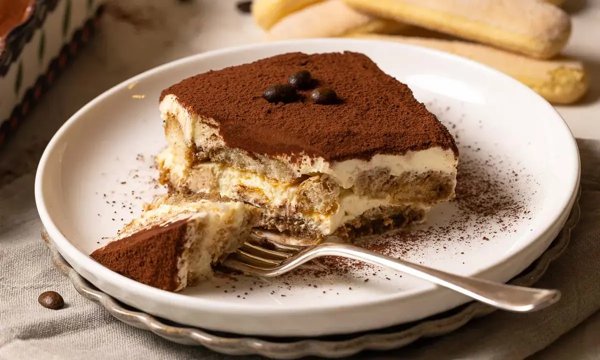 Ein Stück cremiges Tiramisu, bestäubt mit Kakao, wartet auf dich. Dieses Tiramisu Rezept ist ein Genuss!