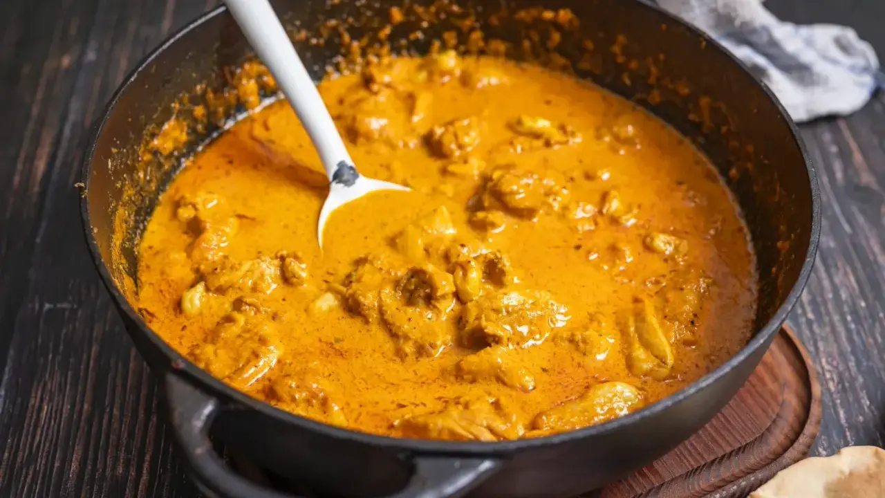 Cremiger Butter Chicken in einer Pfanne, bereit zum Servieren. Ein Löffel ragt aus der köstlichen Sauce.