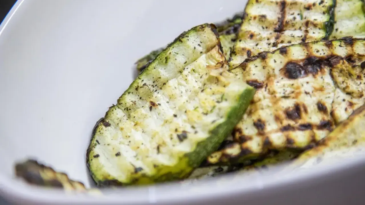 Gegrillte Zucchinischeiben mit Kräutern und Gewürzen in einer weißen Schüssel. Eine köstliche Zucchini Pfanne.