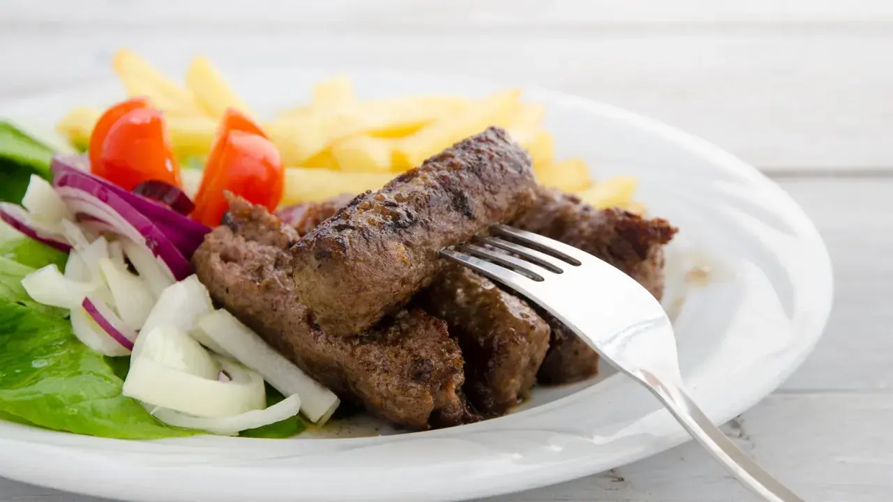 Saftige cevapcici mit knusprigen Pommes, garniert mit frischem Salat, Tomaten und Zwiebeln. Ein köstliches Gericht!