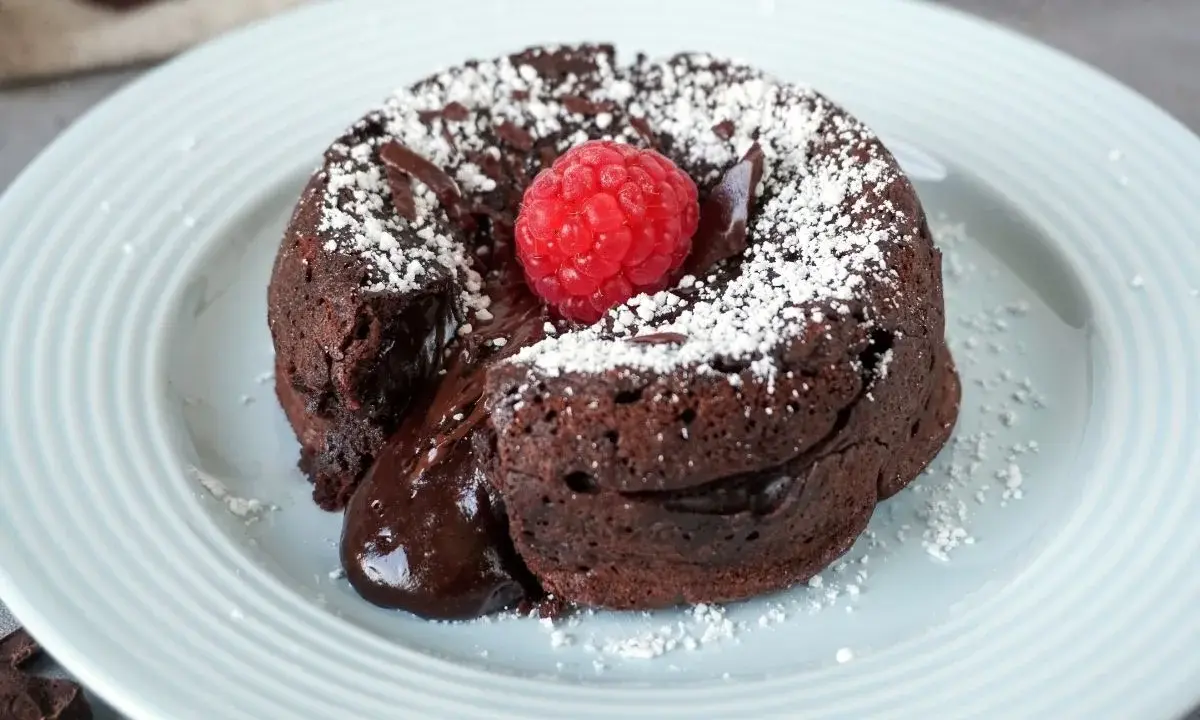 Ein warmer Schokoladenkuchen, ein Coulant de Chocolate, mit flüssigem Kern, garniert mit einer Himbeere und Puderzucker.