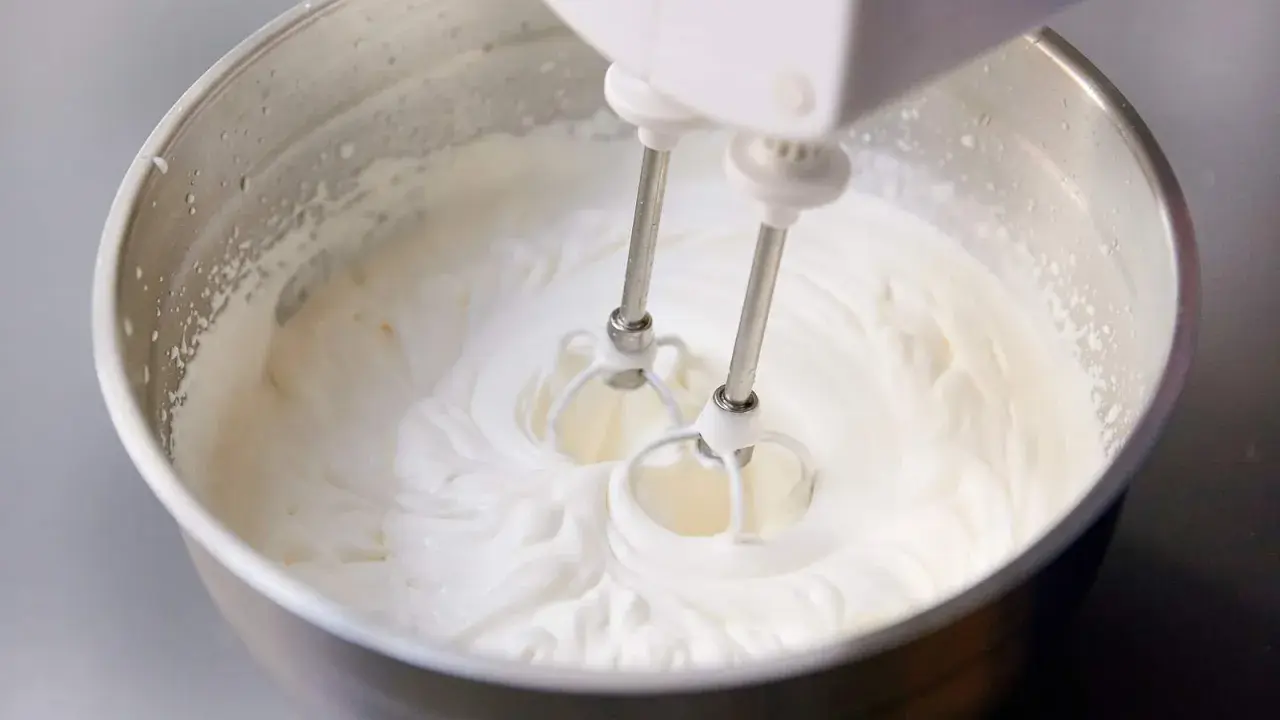 Ein Handmixer schlägt Kochsahne in einer Edelstahlschüssel zu steifer Masse.