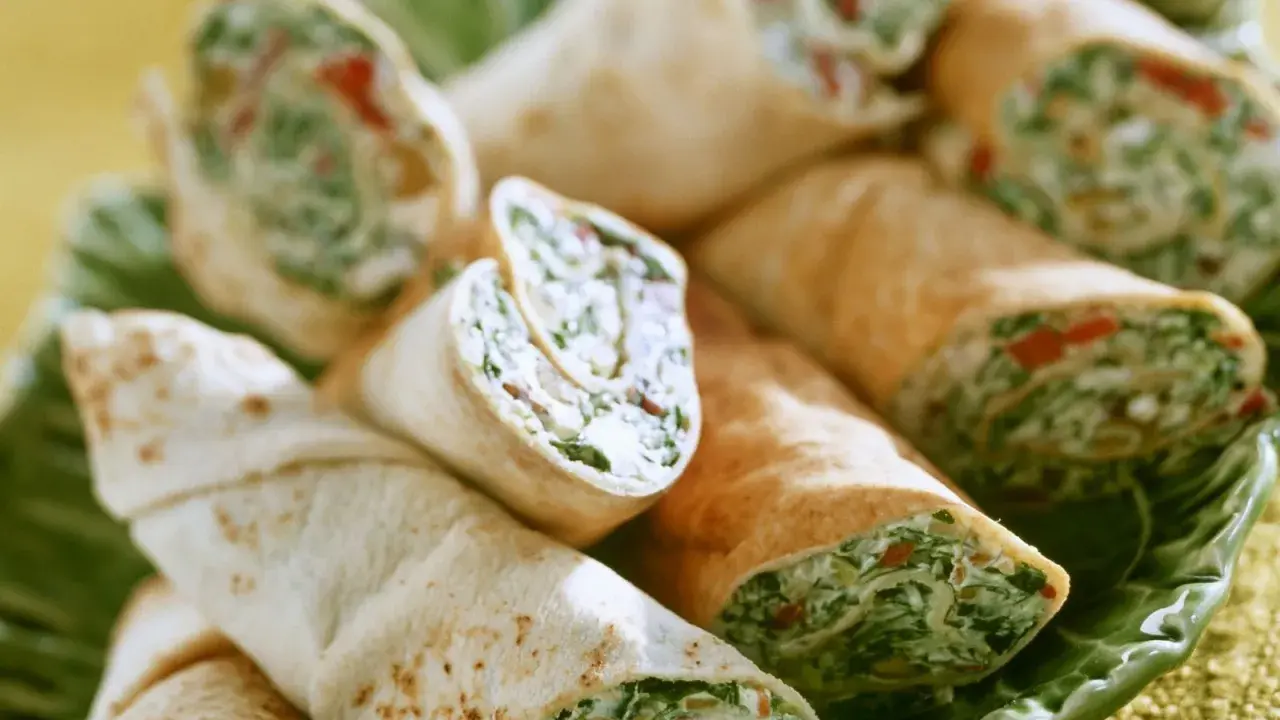 Gerollte Tortilla-Wraps mit Spinat und Feta, appetitlich auf einem grünen Blatt serviert.