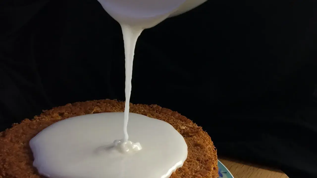 Ein Kuchen wird mit zuckerguss mit milch überzogen. Der flüssige Guss fließt langsam auf die runde Kuchenoberfläche.