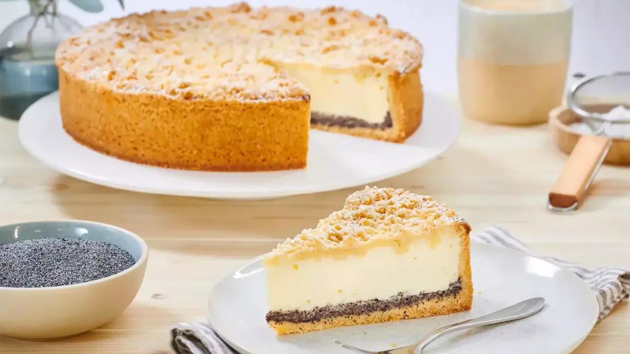 Ein köstlicher Mohn Schmand Kuchen mit Streuseln und Puderzucker. Daneben eine Schale Mohn und eine Tasse Kaffee.