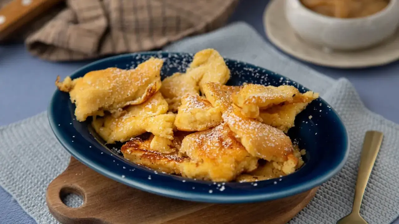 Kaiser­sch­marrn, ein Klassiker der besten Thermomix Rezepte, bestäubt mit Puderzucker auf einem blauen Teller.