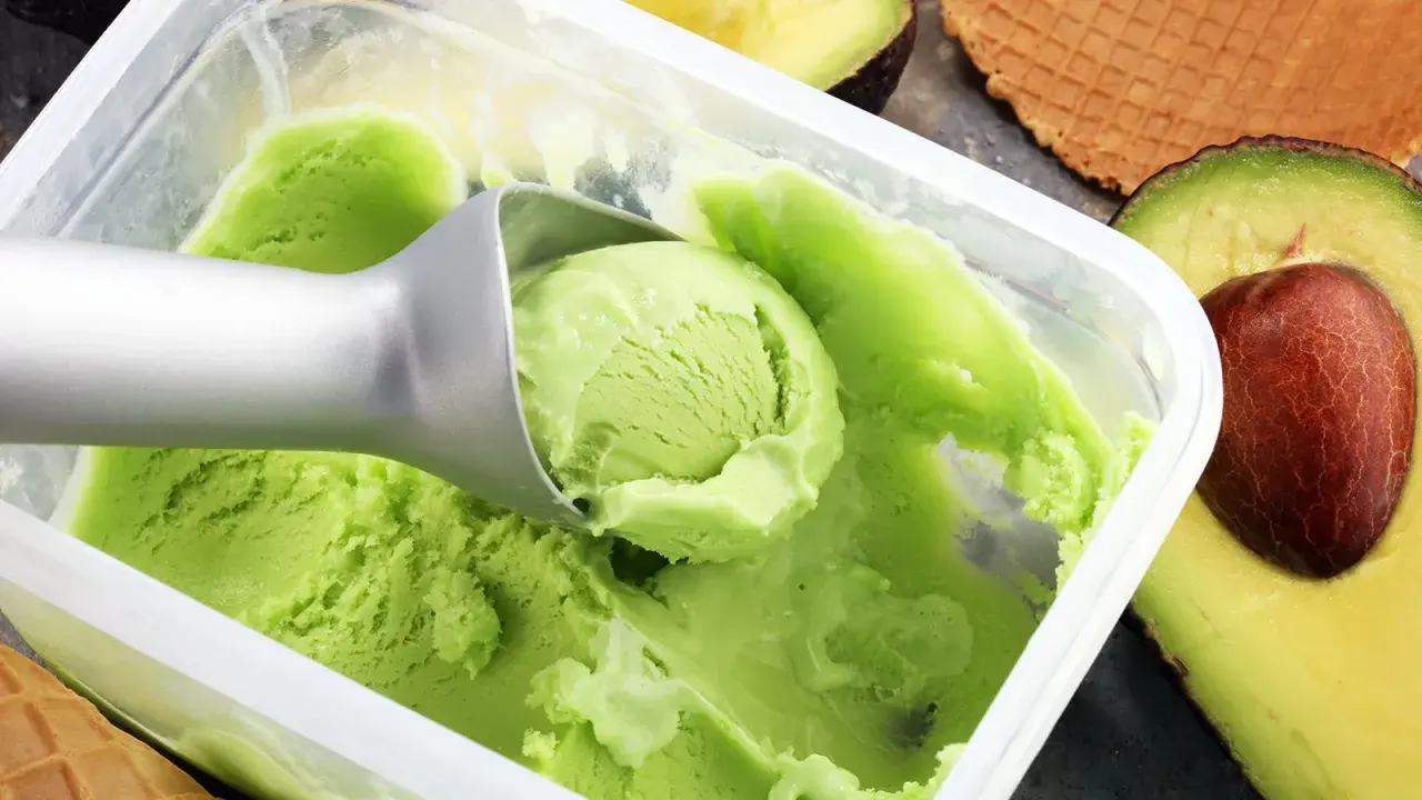 Cremiges, grünes veganes Eis, perfekt zum veganes Eis selber machen mit Mandelmilch. Avocados und Waffeln im Hintergrund.