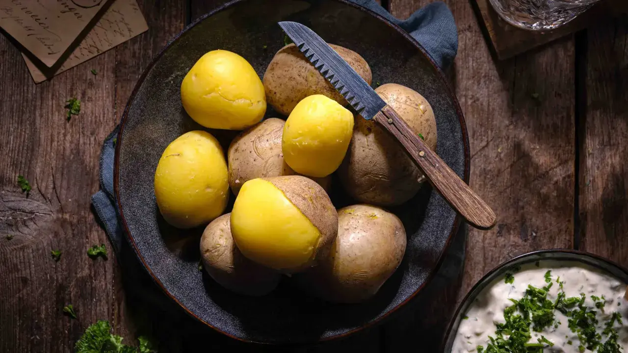 Gekochte und rohe Kartoffeln liegen in einer Schale, bereit für ein deftiges Essen. Ein Messer mit Holzgriff liegt daneben.