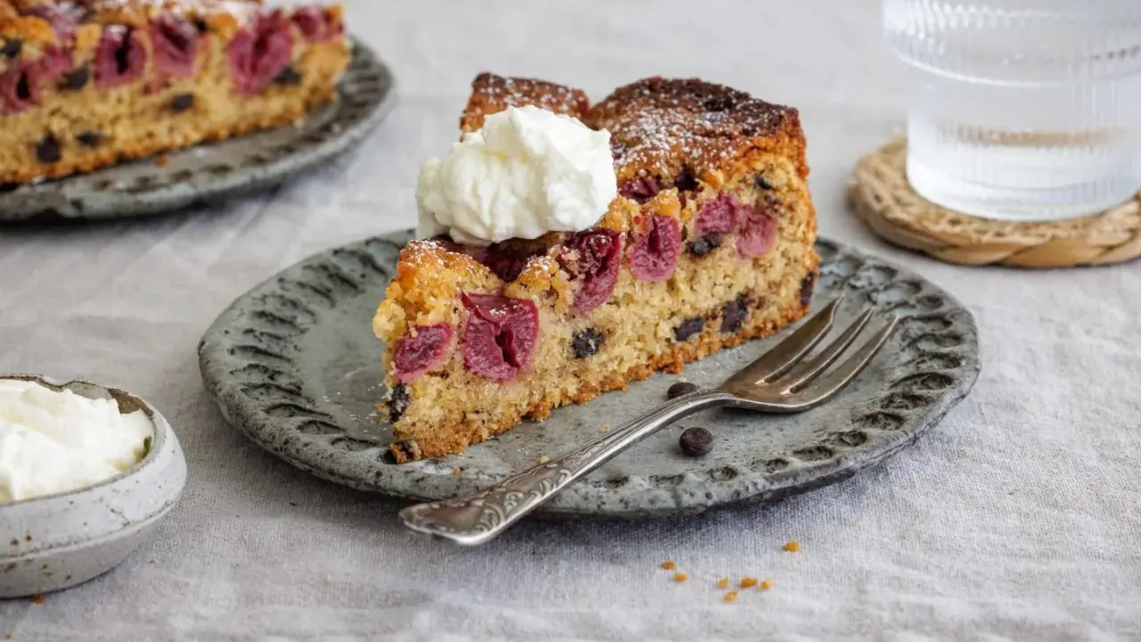 Ein Stück saftiger nusskuchen mit pudding, Kirschen und Schokostückchen, garniert mit Sahne.