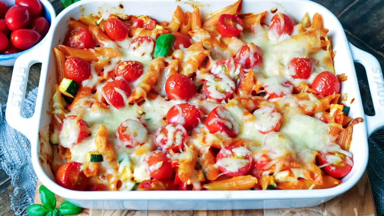 Ein köstlicher nudelauflauf vegetarisch mit Penne, Kirschtomaten und geschmolzenem Käse in einer weißen Auflaufform.