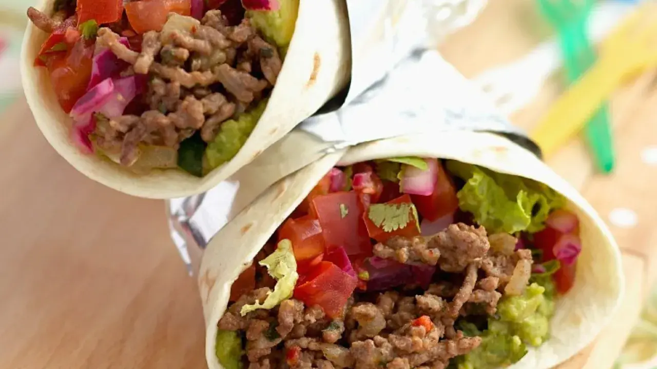 Zwei leckere wraps mit hackfleisch, Guacamole, Tomaten und roten Zwiebeln, eingewickelt in Folie.