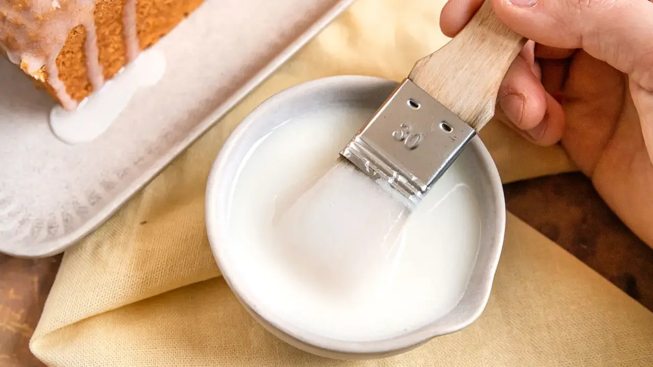 Ein Pinsel taucht in eine Schüssel mit zuckerguss, bereit, einen warmen oder kalten Kuchen zu verfeinern.