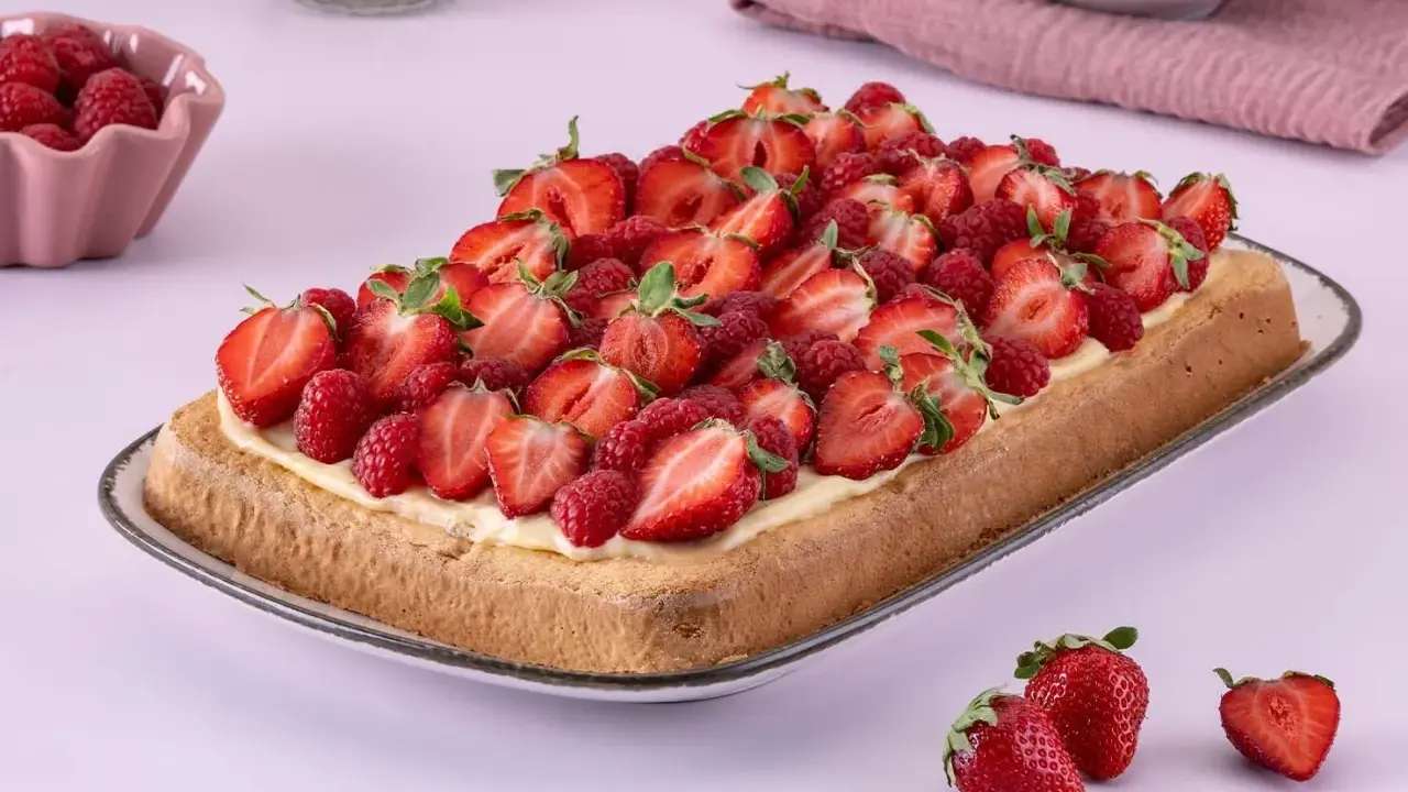 Ein rechteckiger Biskuit-Erdbeerkuchen vom Blech, üppig belegt mit frischen Erdbeeren und Himbeeren auf einer cremigen Schicht.