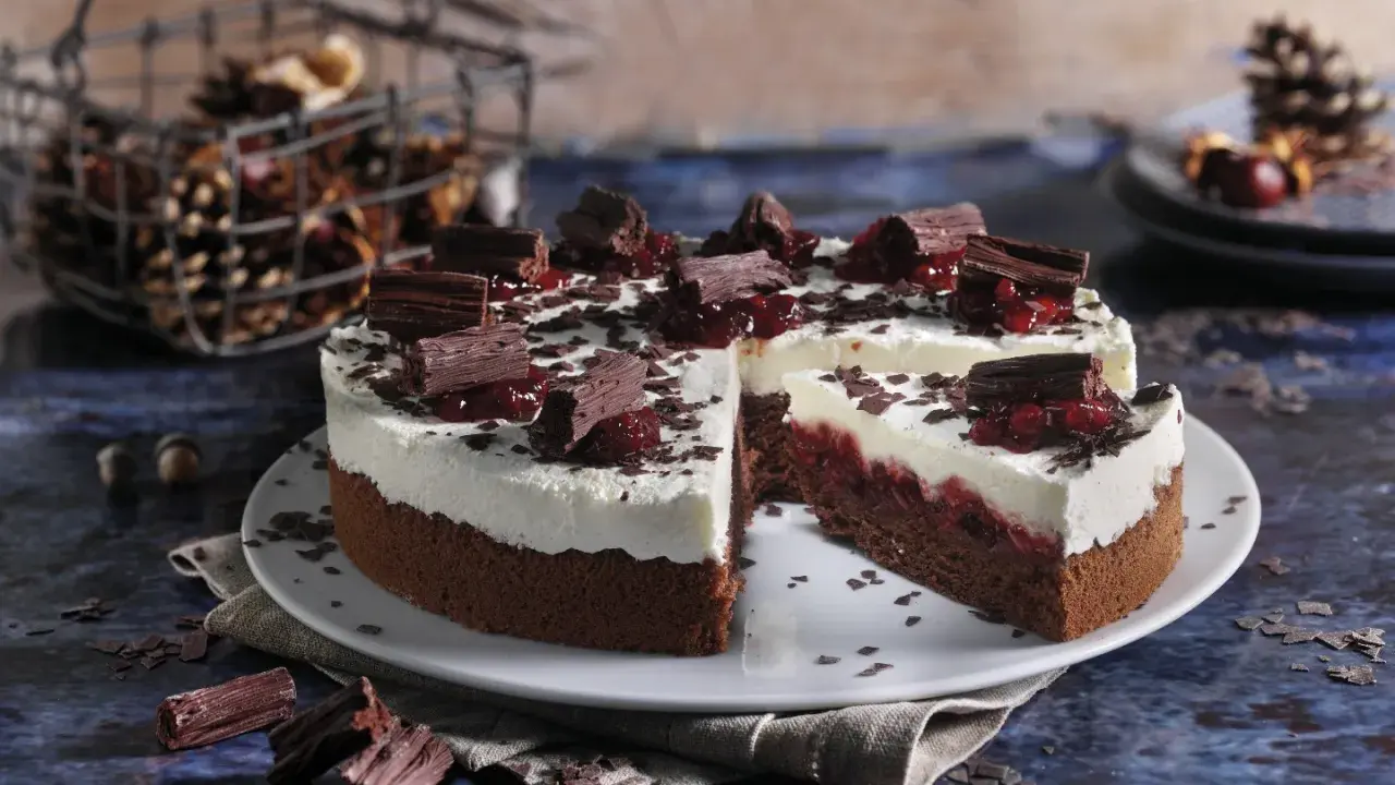 Schokoladen-Sahne-Torte mit Preiselbeeren und Schokostückchen, dekoriert mit Schokoraspeln. Ein Stück ist angeschnitten.