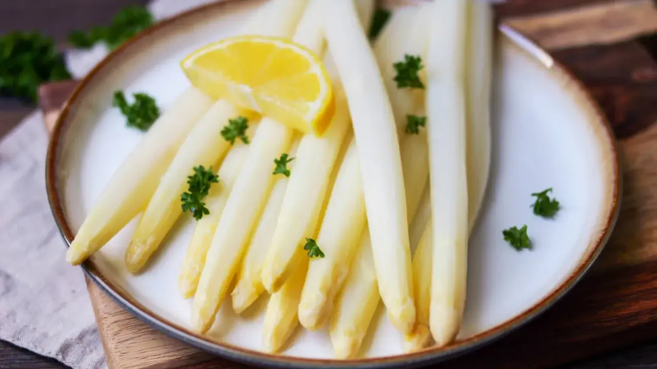 Frischer weißer Spargel, perfekt gegart, liegt auf einem Teller, garniert mit Petersilie und einer Zitronenspalte.