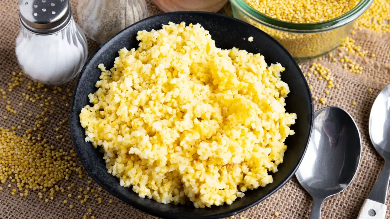 Goldhirse kochen: Ein Teller mit dampfender Hirse, daneben Salz- und Pfefferstreuer, Löffel und eine Schüssel voller ungekochter Hirse.
