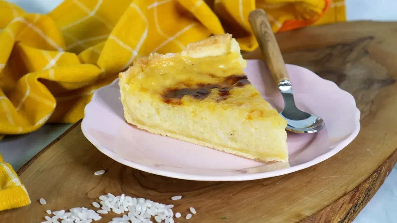Ein Stück cremiger Milchreiskuchen auf rosa Teller, daneben roher Reis. Ein leckeres Milchreiskuchen Rezept zum Nachbacken.