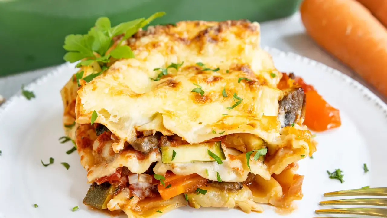 Ein Stück herzhafte vegetarische Lasagne mit geschmolzenem Käse und frischer Petersilie, daneben Karotten.