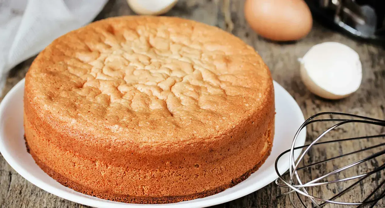 Ein goldbrauner Biskuitboden, perfekt für jedes biskuitboden rezept. Eier und Schneebesen deuten auf die Zubereitung hin.