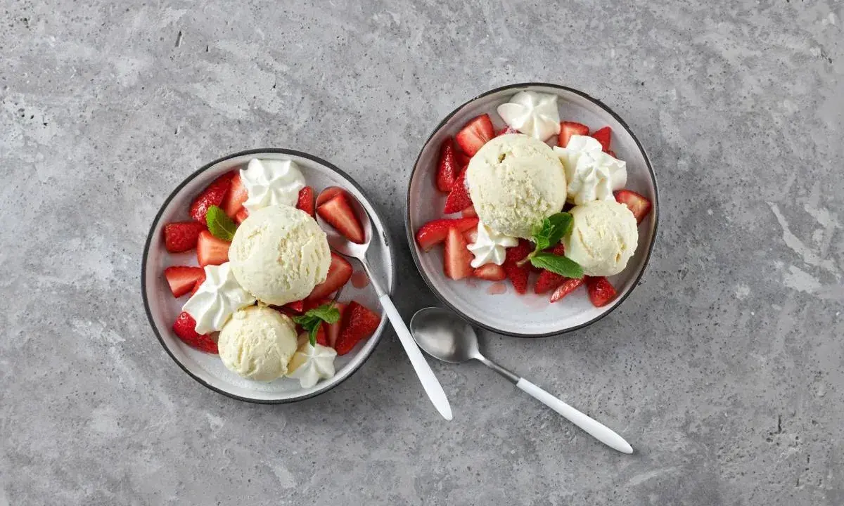 Zwei Schalen mit Erdbeeren Romanoff: frische Erdbeeren, cremiges Eis und Schlagsahne, garniert mit Minze.