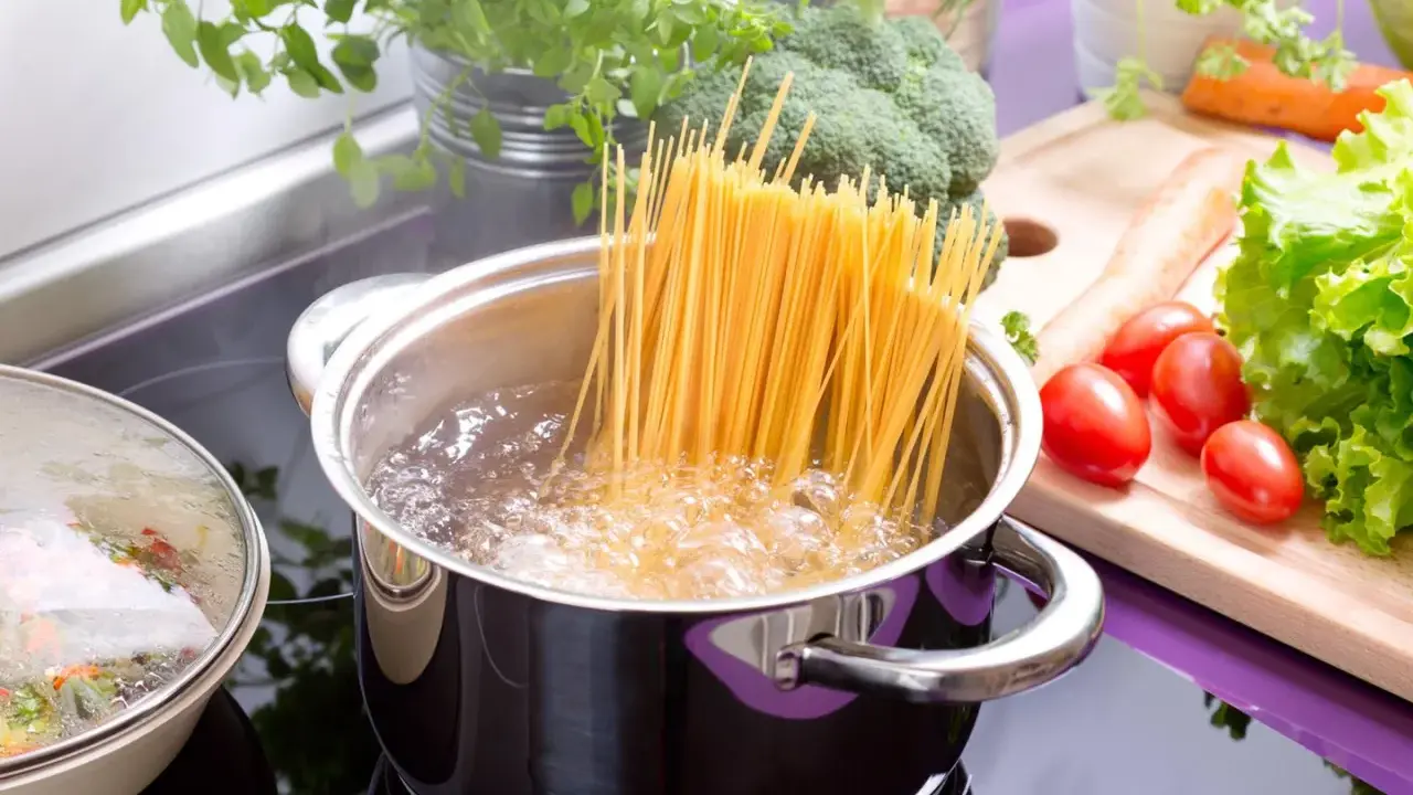 Spaghetti kochen: Lange Nudeln werden in kochendes Wasser gegeben. Frisches Gemüse wie Brokkoli, Karotten und Tomaten liegen bereit.