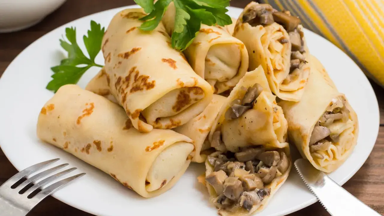 Herzhafte Pfannkuchen gefüllt mit Pilzen und Zwiebeln, garniert mit Petersilie, auf einem weißen Teller mit Gabel und Messer.