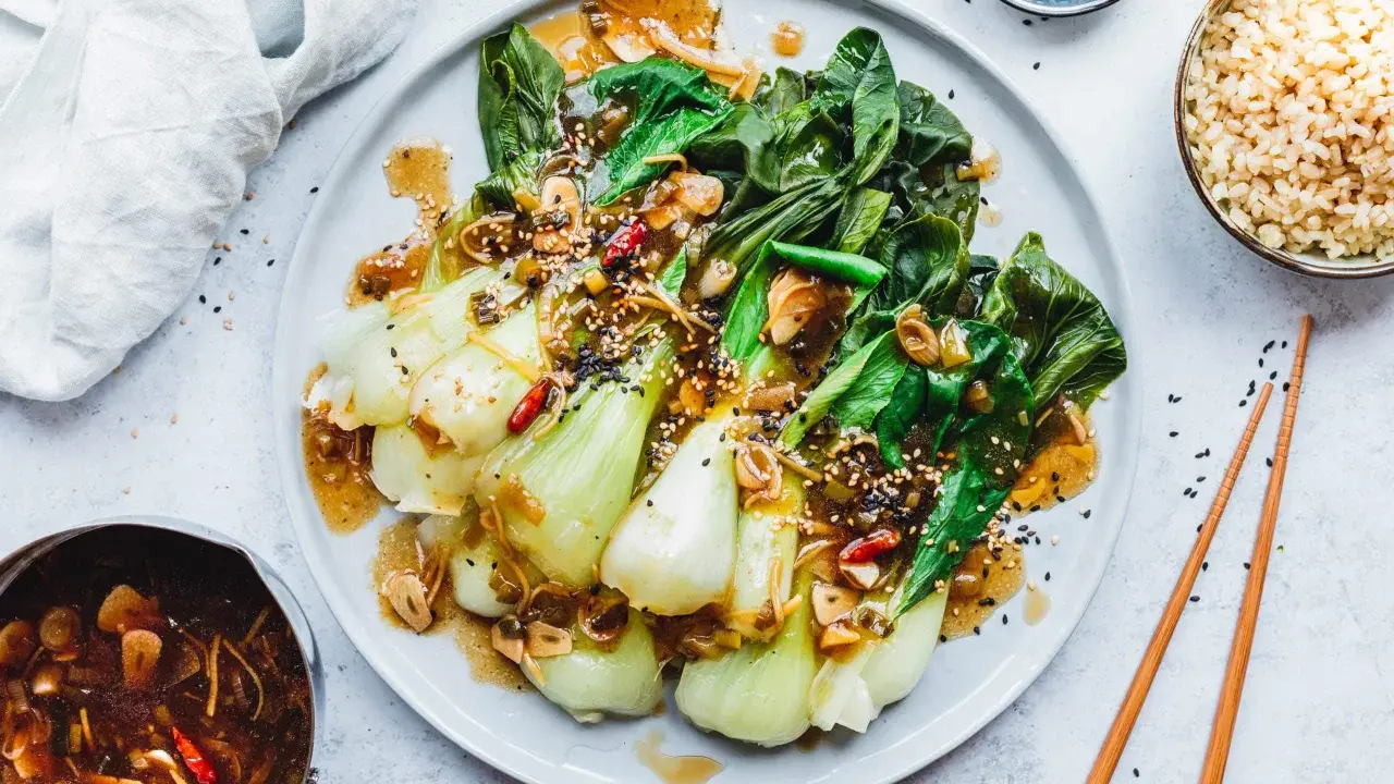 Ein Teller mit gebratenem Pak Choi, garniert mit Sesam und Chili, serviert mit Reis und einer Sauce.