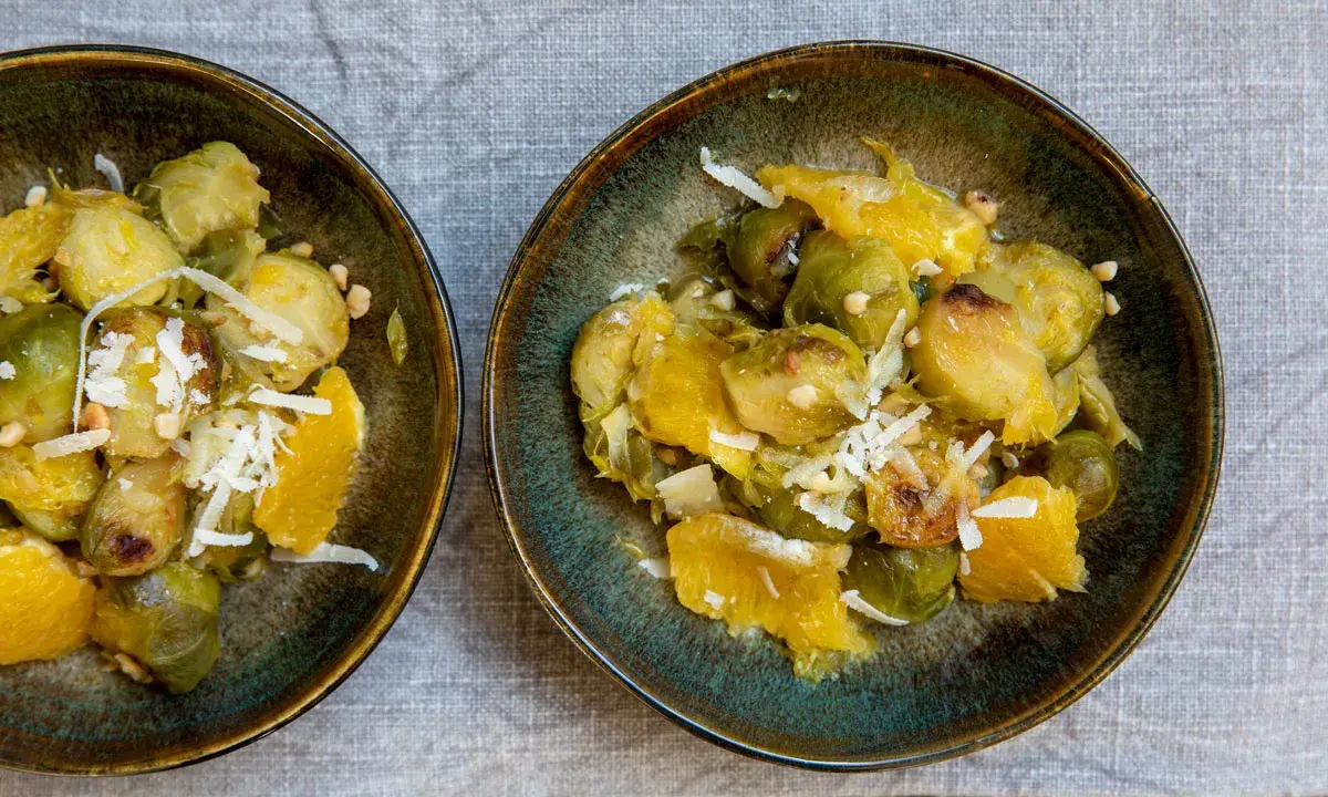 Zwei Schalen mit Rosenkohl, Orangenstücken und geriebenem Käse. Ein Gericht, das an ewiger Kohl Rezepte erinnert.