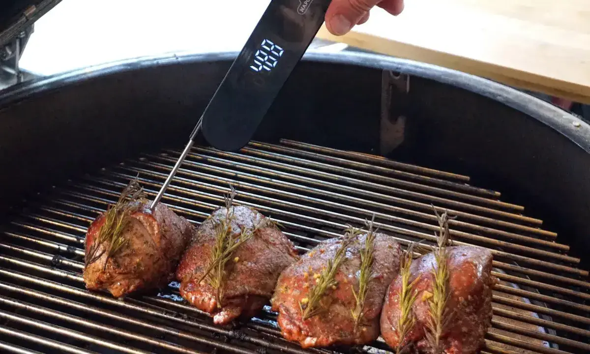 Vier Hirschsteaks mit Rosmarin auf dem Grill, ein Thermometer zeigt 48°C an. So gelingt das Hirschsteak richtig braten.