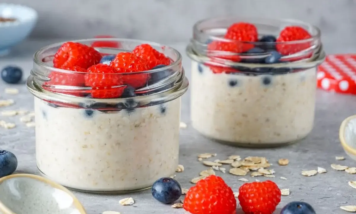 Zwei Gläser mit Overnight Oats, garniert mit frischen Himbeeren und Blaubeeren. Perfekt für ein gesundes Frühstück.