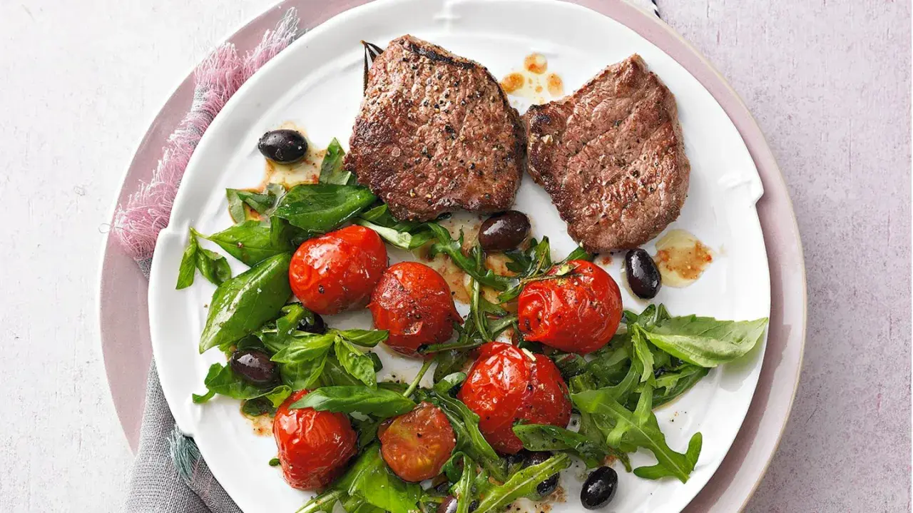 Zwei saftige Minutensteaks im Backofen zubereitet, serviert mit gerösteten Kirschtomaten, Rucola und schwarzen Oliven.