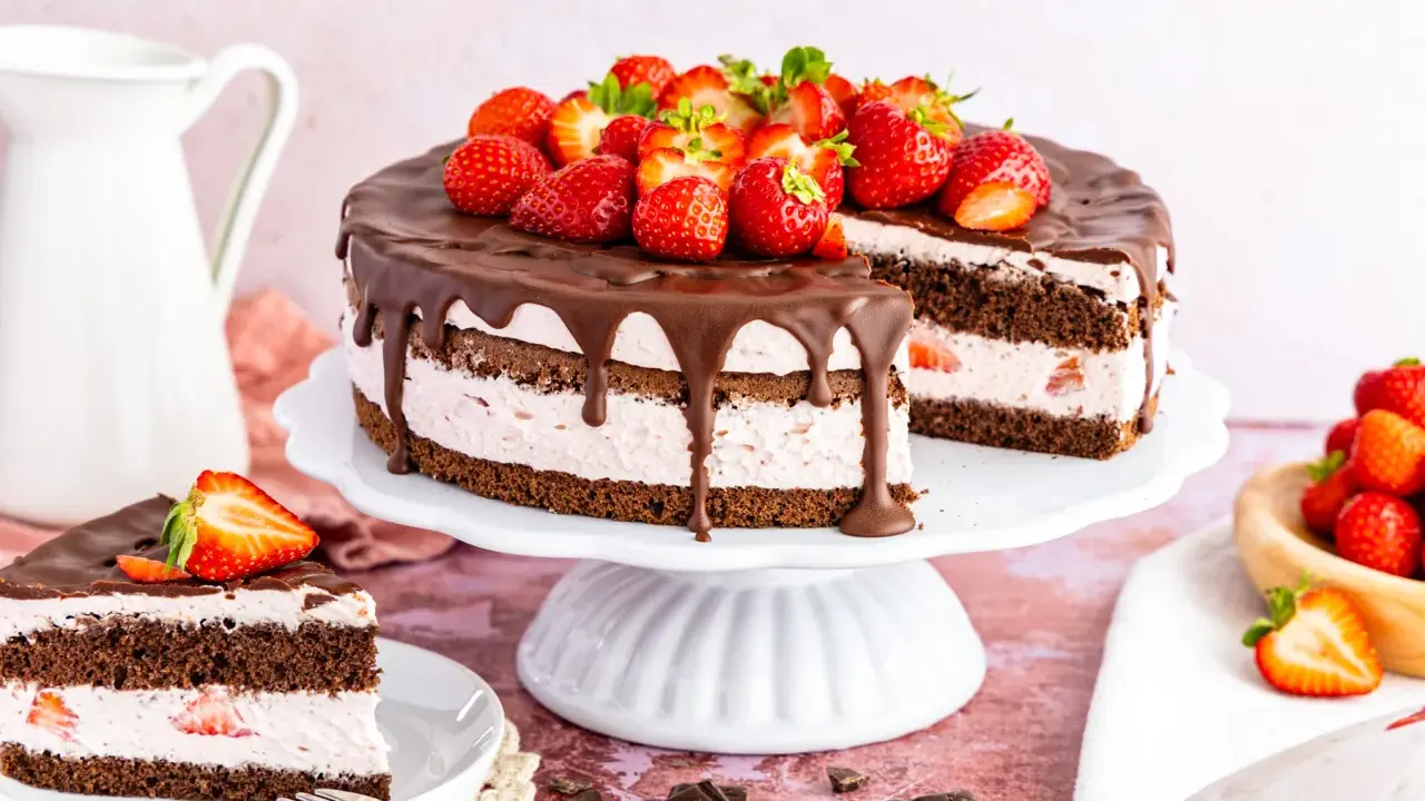 Ein saftiger Erdbeerkuchen mit Schokolade, dekoriert mit frischen Erdbeeren und Schokoladenglasur. Ein Stück ist bereits angeschnitten.