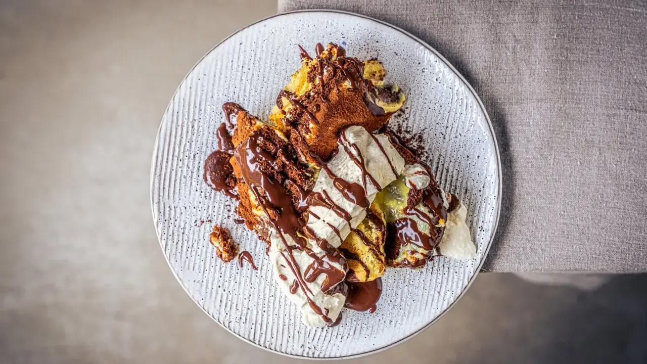 Ein köstlicher Somlauer Nockerl-Dessert auf einem Teller, mit Schokoladensauce und Eiscreme garniert.
