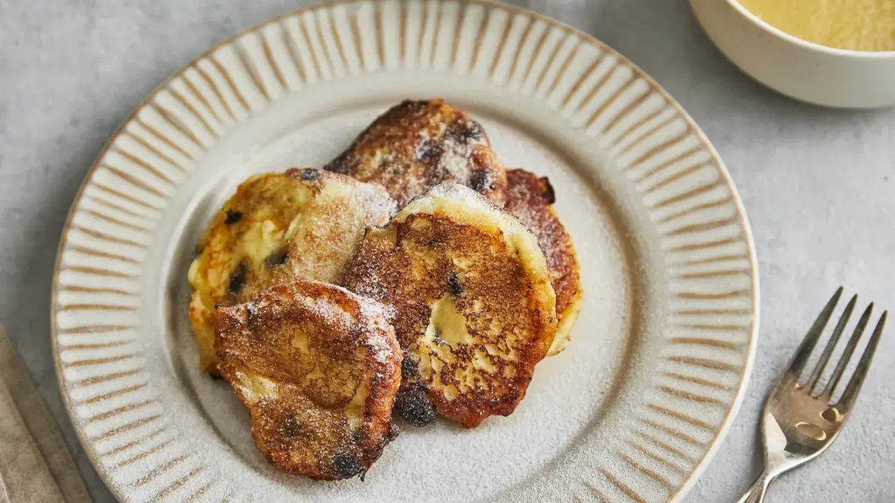 Goldbraune Quarkkeulchen mit Zucker bestreut auf dunklem Teller, daneben Apfelmus und Besteck.