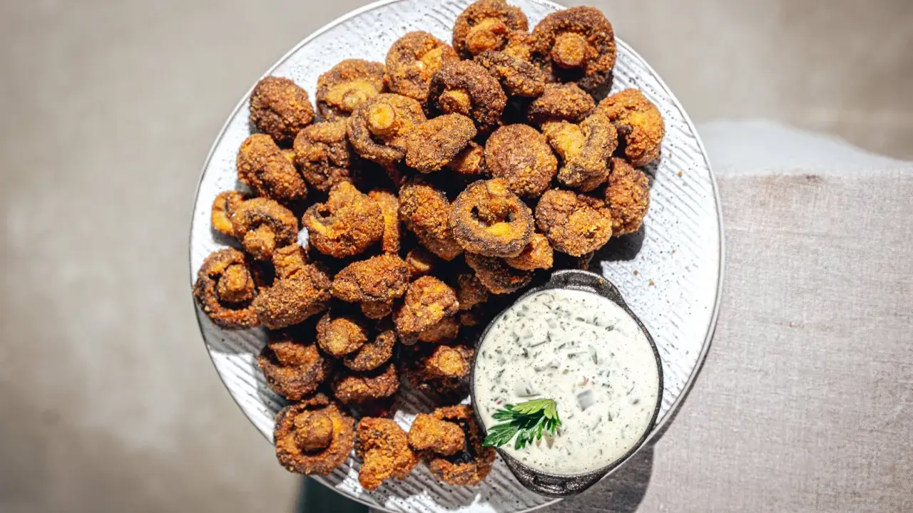Knusprig gebackene Champignons auf einem Teller, daneben eine Schale cremiger Dip mit Kräutern. Ein Genuss!