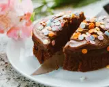 Schokoladenkuchen mit bunter Streusel-Deko, ein köstliches Dessert, um Kuchenreste zu verwerten. Daneben zarte rosa Blüten.