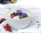 Joghurt mit Beeren und leinsamen, beträufelt mit Honig. Blaue Kornblumen zieren die Schüssel.