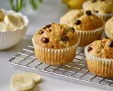 Frisch gebackene schoko bananen muffins mit Schokostückchen auf einem Gitter. Daneben eine Schüssel mit Bananenscheiben.